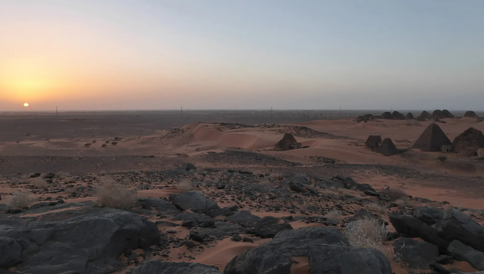 Open desert at dusk with pyramids on the horizon